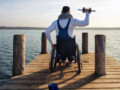 Young male wheelchair user on a pier exercising with a weight in his right hand.